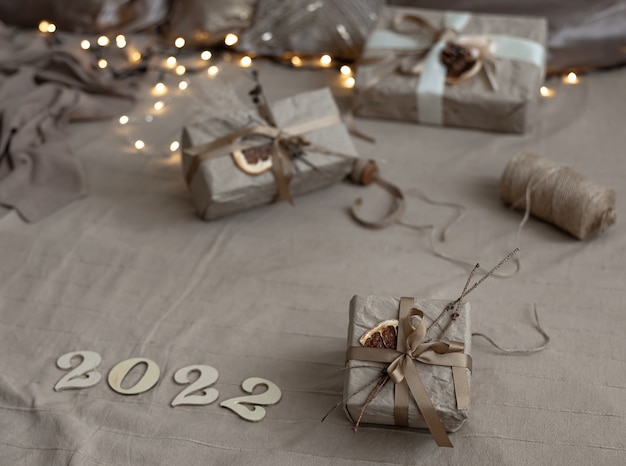 Christmas background with gift boxes wrapped in craft paper and wooden numbers 2022 on blurred background with garland.