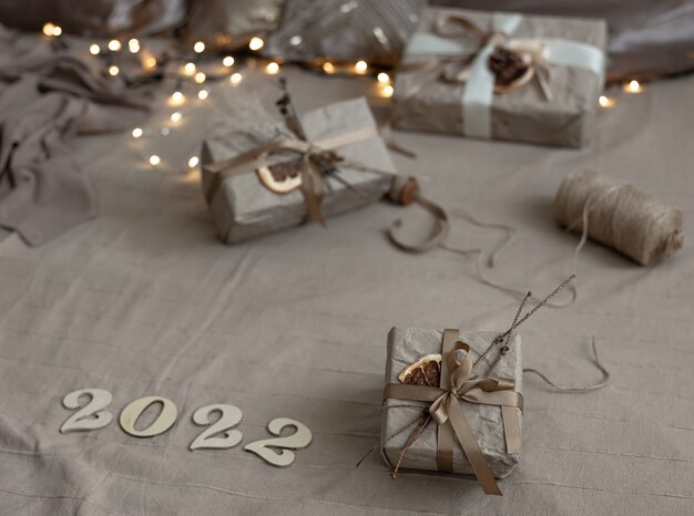 Christmas background with gift boxes wrapped in craft paper and wooden numbers 2022 on blurred background with garland.