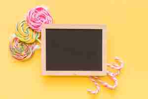 Free photo christmas candy canes and lollipops behind the wooden slate over the yellow background