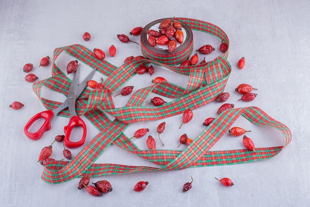 Christmas candy colored ribbons and dog rose fruits on white background.