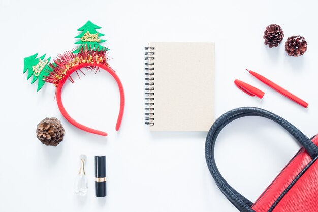 Christmas composition. Christmas fashion for girl, cosmetics, bag, pine cones, notebook and red pen with copy space. Flat lay, top view