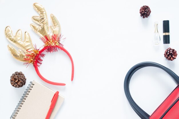 Christmas composition. Christmas fashion for girl, cosmetics, bag, pine cones, notebook and red pen with copy space. Flat lay, top view