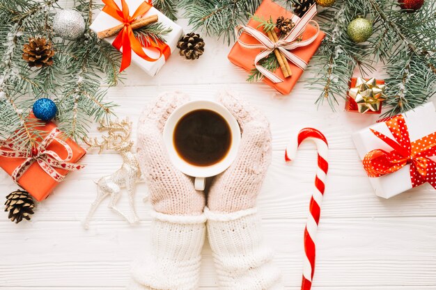 Christmas composition with hands wearing gloves touching coffee cup