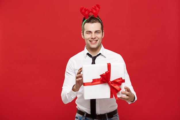 Christmas Concept Cheerful happy young businessman with a decorative gift isolated on red background