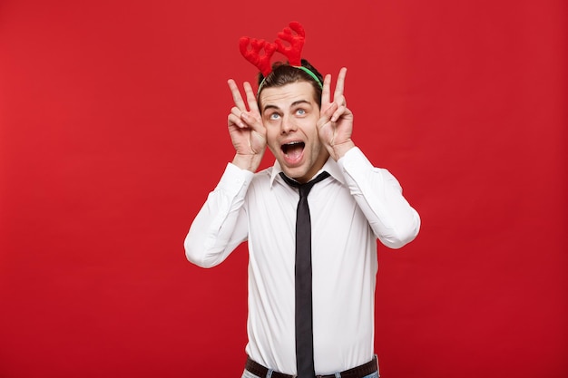 Foto gratuita concetto di natale il bell'uomo d'affari celebra il buon natale e il felice anno nuovo indossa la fascia per capelli con le renne e tiene il gesto del coniglio