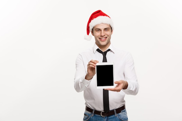 Concetto di natale l'uomo d'affari bello presenta qualcosa sullo schermo mobile festeggia il buon natale e il felice anno nuovo indossa il cappello di babbo natale