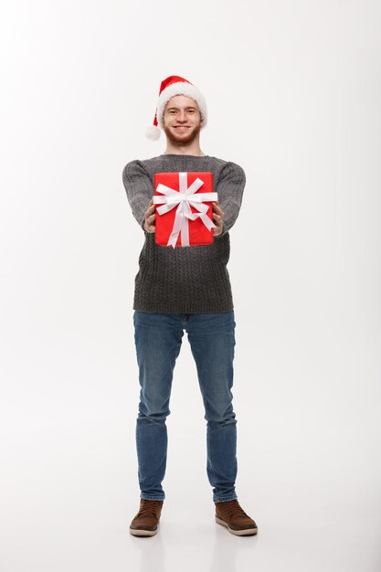 クリスマスのコンセプト白い背景で隔離のカメラにプレゼントを与えるひげを持つ幸せな若いハンサムな男
