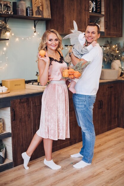 Christmas concept photo of joyful little family of husband, wife and baby posing in well-furnished kitchen. Holiday concept