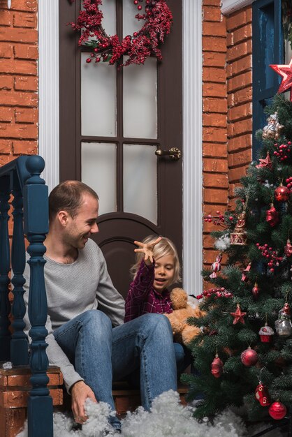 Christmas concept with father and daughter sitting in front of house