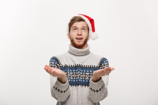 クリスマスのコンセプト雪のジェスチャーを待っているセーターの若いクールなひげの男