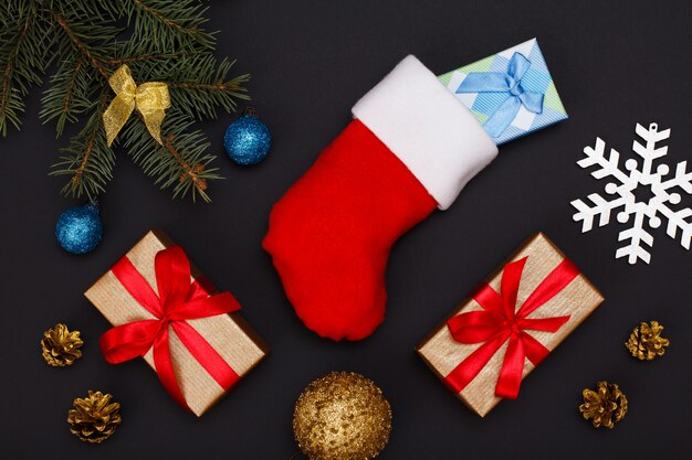 크리스마스 장식. 산타의 부츠, 선물 상자, 원뿔이 있는 전나무 나뭇가지와 검은 배경에 크리스마스 장난감. 평면도. 크리스마스 인사말 카드 개념입니다.