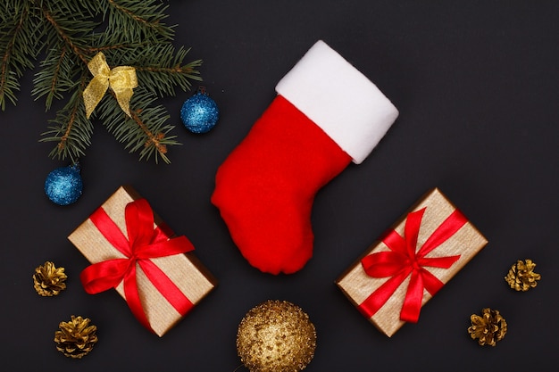 크리스마스 장식. 산타의 부츠, 선물 상자, 검은 배경에 콘과 크리스마스 장난감이 있는 천연 전나무 가지. 평면도. 크리스마스 인사말 카드 개념입니다.