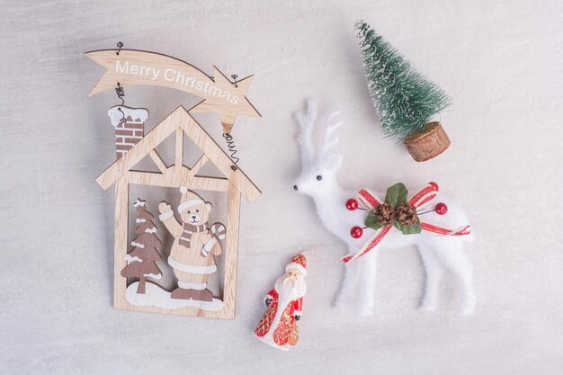 Christmas decorations, toy deer, pine tree and Santa on white surface.