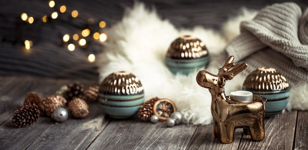 Christmas festive background with toy deer with a gift box, blurred background with golden lights, festive background on wooden deck table