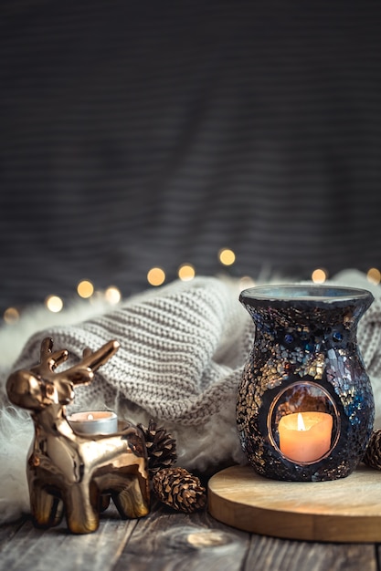 Christmas festive composition with toy deer, golden lights and candles on wooden deck table and winter sweater