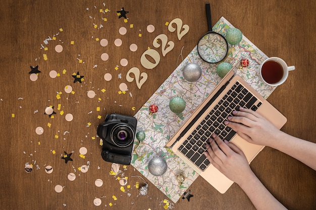 Free photo christmas festive travel flat lay with numbers 2022, map, camera and laptop on wooden background.