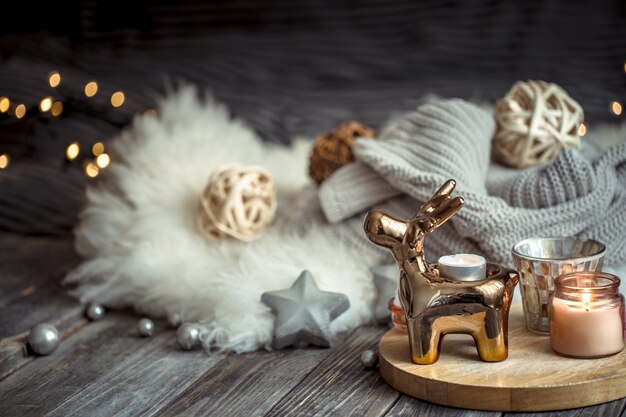 おもちゃの鹿のクリスマスのお祝いの壁、金色のライトとキャンドルのぼやけた壁、木製デッキテーブルのお祝いの壁