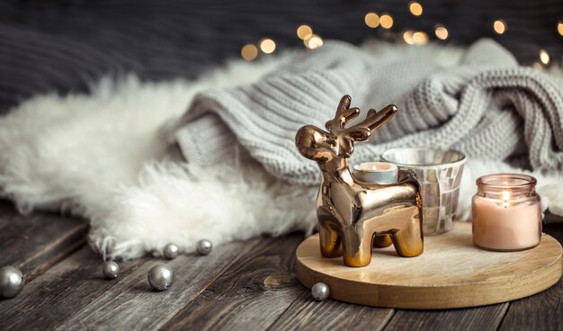 Christmas festive wall with toy deer, blurred wall with golden lights and candles, festive wall on wooden deck table