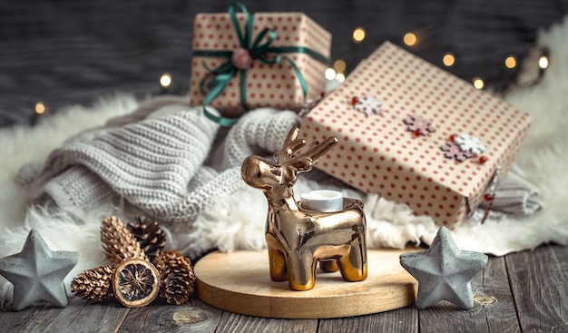 Рождественская праздничная стена с игрушечным оленем с подарочной коробкой и елкой, размытая стена с золотыми огнями на деревянном столе