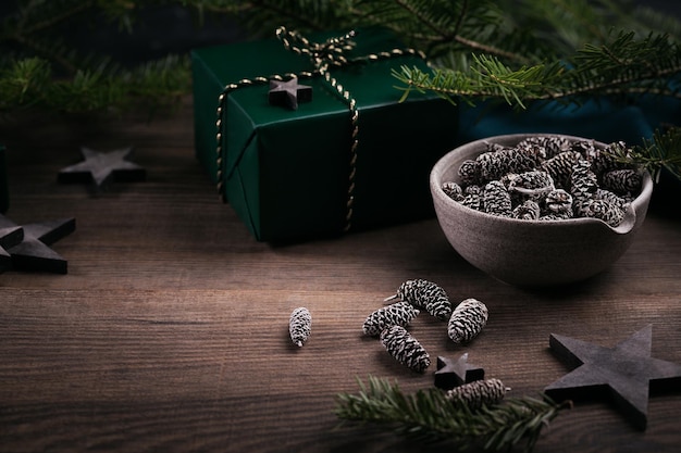 緑のギフトボックス、木製の星の装飾、暗い木製の背景にモミの円錐形とトウヒの枝が付いたクリスマスフレーム。自然な地球の色の休日の背景。 Premium写真