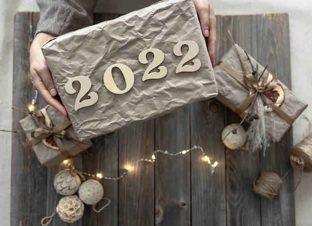 Christmas gift box with wooden numbers 2022 in female hands against the backdrop of festive decor.