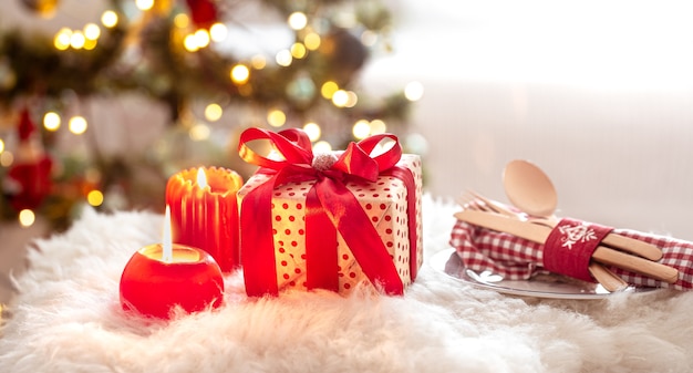 Christmas gift, cutlery set and plate with candles on blurred bokeh background close up.