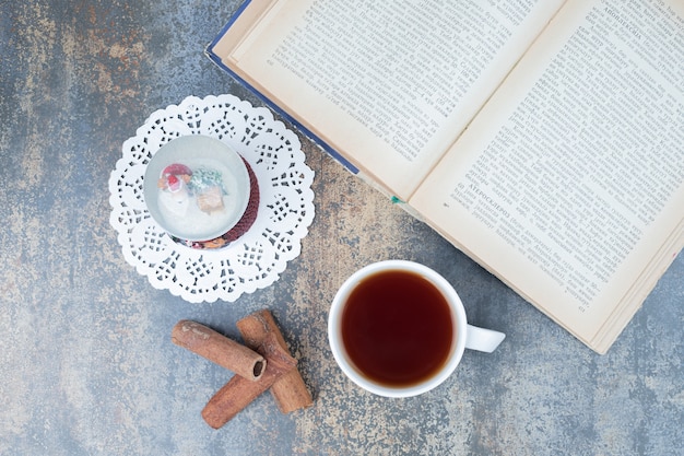 Free photo christmas globe, cup of tea and open book on marble surface. high quality photo