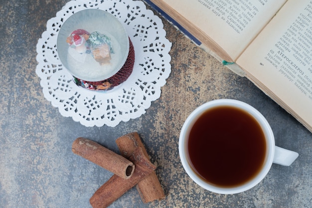 Christmas globe, cup of tea and open book on marble surface. High quality photo