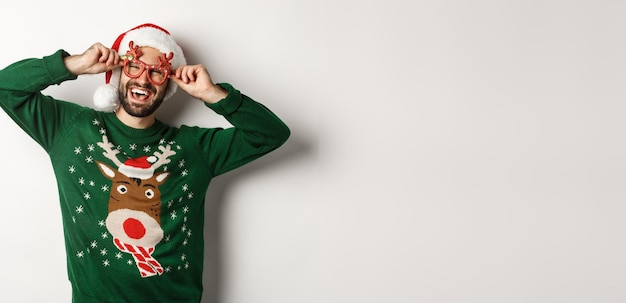 Foto gratuita concetto di celebrazione delle vacanze di natale uomo felice con cappello da babbo natale e occhiali da festa divertenti in piedi di nuovo