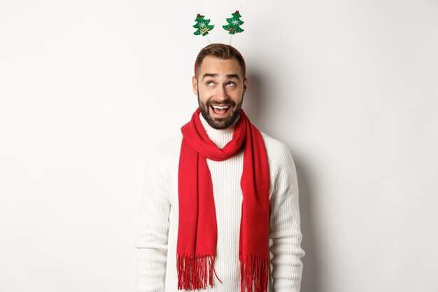 クリスマス休暇。冬の休日を祝う興奮した男、新年のパーティーアクセサリーと赤いスカーフを身に着けて、白い背景に立っています。