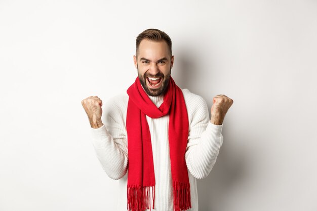 Christmas holidays and New Year concept. Happy man celebrating victory, winning and making fist pumps, achieve goal, saying yes while standing over white background