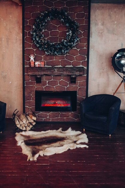 モミの枝で作られたクリスマスリースで飾られたクリスマスのインテリア。電気暖炉の前の床に2つのアームチェアと本物の動物の毛皮。