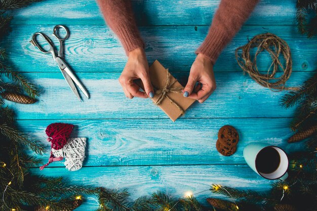 青いwoddenのテーブルのクリスマスの項目。クリスマスプレゼントを包んでいる女性の手。