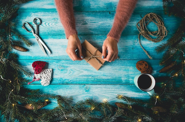 Christmas items on a blue wooden table. Woman's hands wrapping Christmas gift.