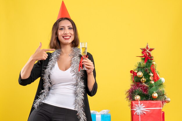 Christmas mood with confused beautiful lady holding and pointing wine in the office on yellow 