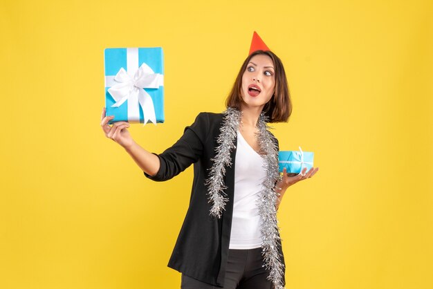 Christmas mood with emotional business lady with xsmas hat holding gifts on yellow 