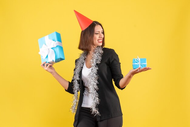 Christmas mood with positive business lady in suit with xsmas hat looking at her gifts on yellow 