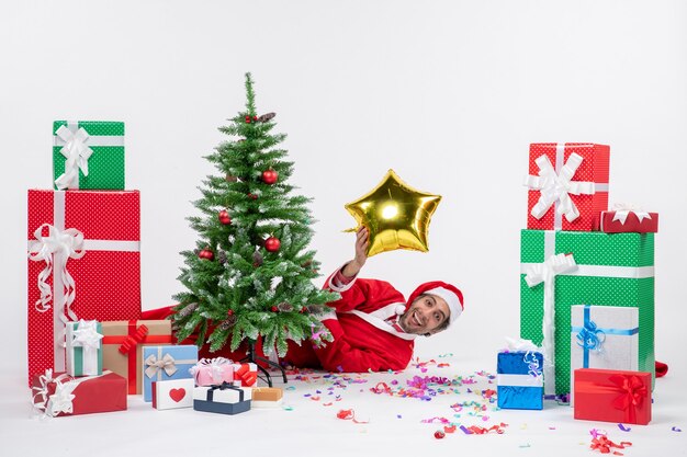 Christmas mood with santa claus lying behind christmas tree near gifts in different colors on white background