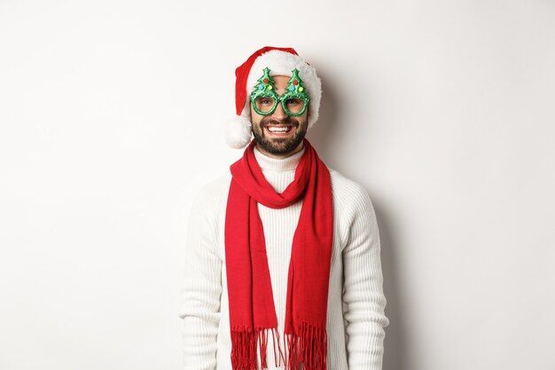 크리스마스, 새 해 및 축 하 개념입니다. 행복 한 남자 웃 고, 산타 모자와 파티 안경을 쓰고 흰색 배경 위에 서