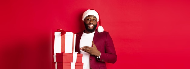 Free photo christmas new year and shopping concept cheerful black man secret santa holding xmas presents and sm