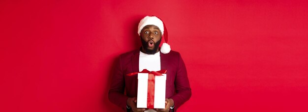 Natale, capodanno e concetto di shopping hanno sorpreso l'uomo afroamericano con il cappello di babbo natale dicendo wow holdi