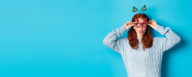 Foto gratuita festa di natale e concetto di celebrazione ragazza rossa sciocca che si gode il nuovo anno indossando occhiali divertenti a