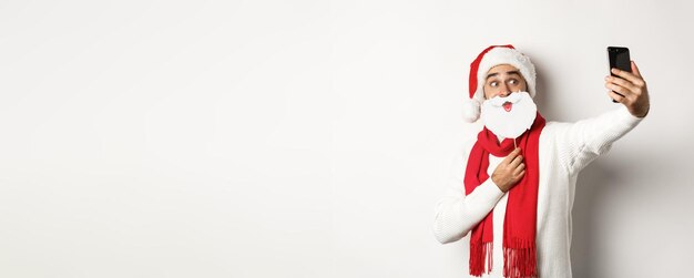 クリスマス パーティーやお祝いのコンセプト若い男面白い白ひげサンタ マスクで selfie を取って、