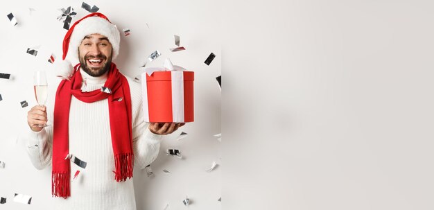 Foto gratuita festa di natale e concetto di vacanze ragazzo felice che celebra il nuovo anno tenendo un regalo e bevendo un bicchiere