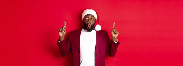 Free photo christmas party and holidays concept impressed black man showing offer pointing fingers up at logo s