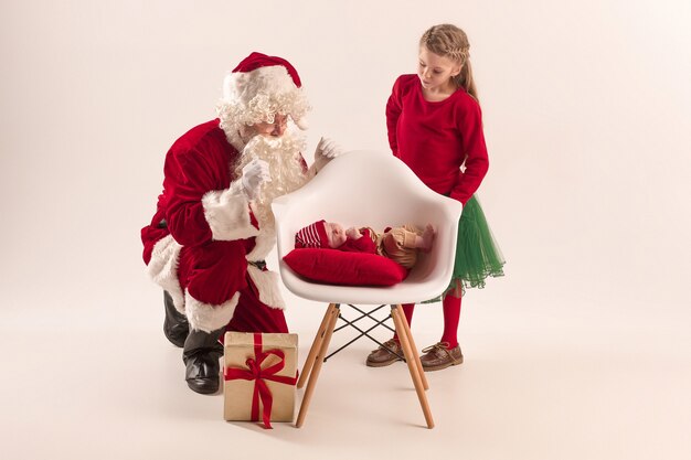 Christmas portrait of cute little newborn baby girl and pretty teen sister dressed in christmas clothes and man wearing santa costume and hat