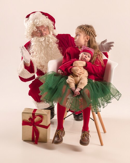 Christmas portrait of cute little newborn baby girl and pretty teen sister dressed in christmas clothes and man wearing santa costume and hat