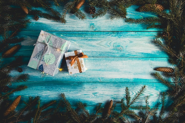 Рождественские подарки на синем деревянном столе с еловыми веточками и рождественскими огнями.