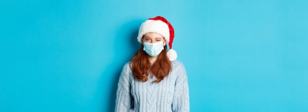 Free photo christmas quarantine and covid concept cheeky redhead female model in face mask and santa hat winkin