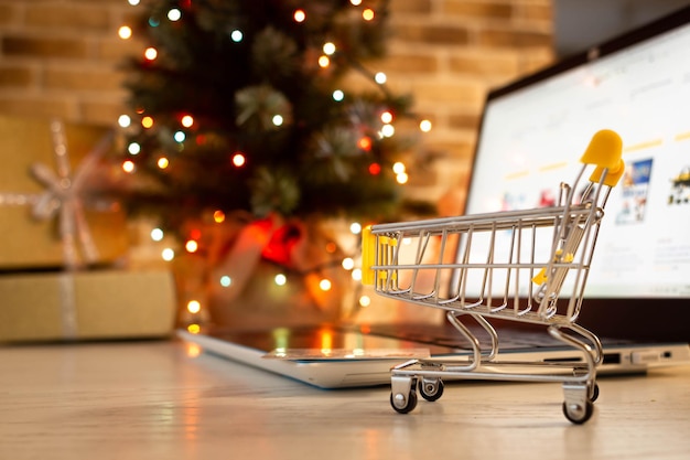 Christmas shopping online. laptop with shopping cart at home on the background of a christmas tree with blurred bokeh lights.